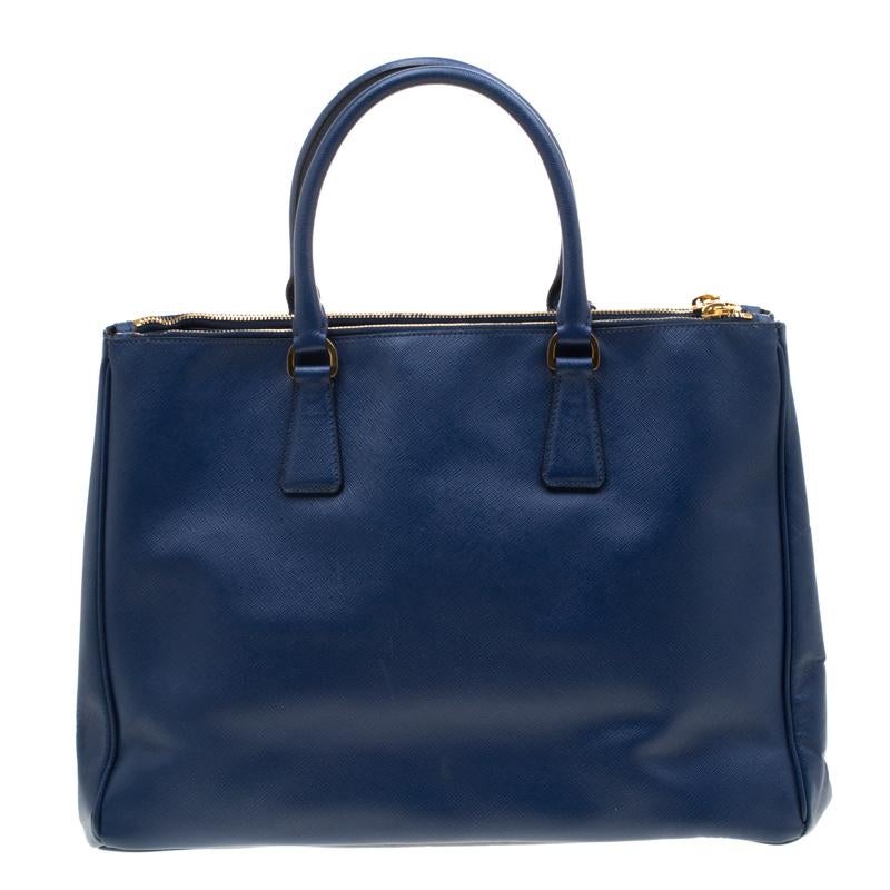 Feminine in shape and grand on design, this Double Zip tote by Prada will be a loved addition to your closet. It has been crafted from the signature Saffiano Lux leather and styled minimally with gold-tone hardware. It comes with two top handles,