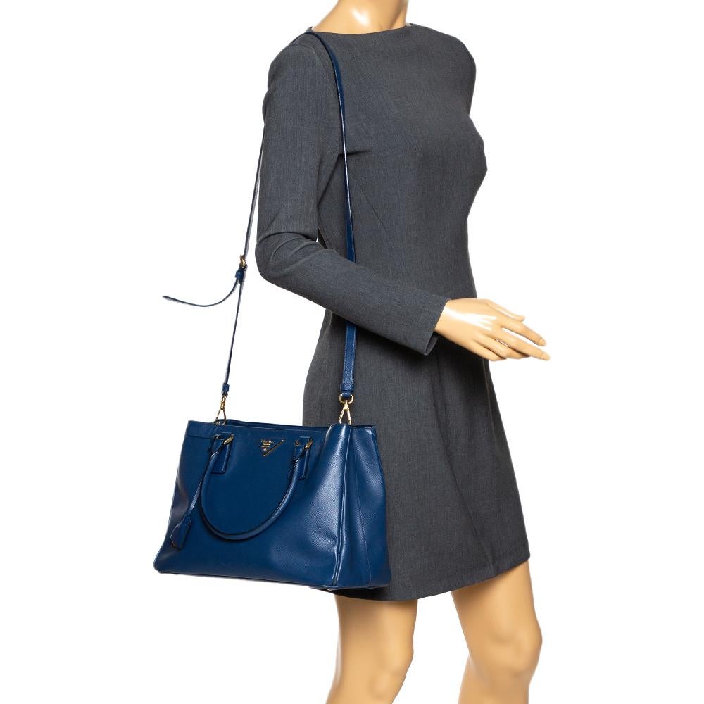 Loved for its classic appeal and functional design, Galleria is one of the most iconic and popular bags from the house of Prada. This beauty in blue is crafted from leather and is equipped with two top handles, the brand logo at the front and a