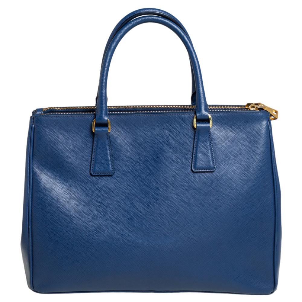 Loved for its classic appeal and functional design, the Galleria tote is one of the most iconic and popular bags from the house of Prada. This beauty in blue is crafted from Saffiano lux leather and is equipped with two top handles and the brand