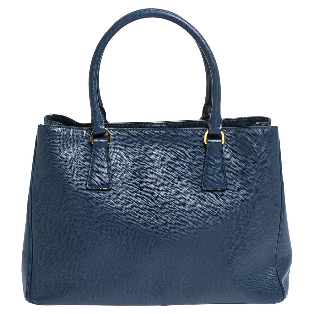 Loved for its classic appeal and functional design, Galleria is one of the most iconic and popular bags from the house of Prada. This beauty in blue is crafted from leather and is equipped with two top handles, the brand logo at the front and a