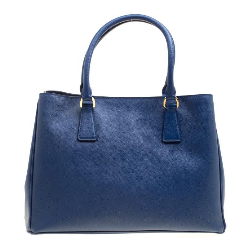 For women with an on-the-go lifestyle, this medium tote from the house of Prada is an elegant option. Masterfully designed, it is rendered in blue Saffiano Lux leather and adorned with gold-tone hardware. The bag opens to an interior lined with