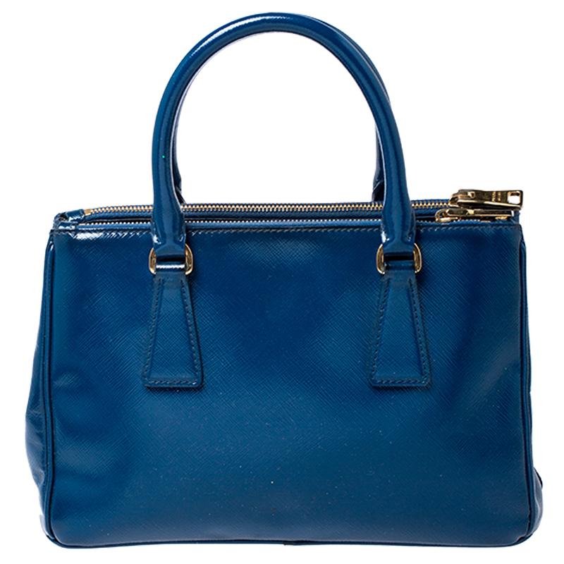Feminine in shape and grand on design, this Double Zip tote by Prada will be a loved addition to your closet. It has been crafted from Saffiano Lux patent leather and styled minimally with gold-tone hardware. It comes with two top handles, two zip