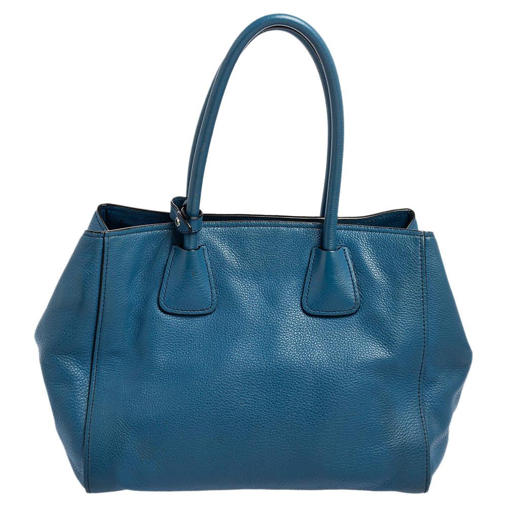 This Front Pocket Wing tote by Prada is an investment-worthy creation. It is constructed using Vitello Daino leather in blue and equipped with two handles, a front zip pocket, and silver-tone hardware. It has a nylon-lined interior with a zip pocket