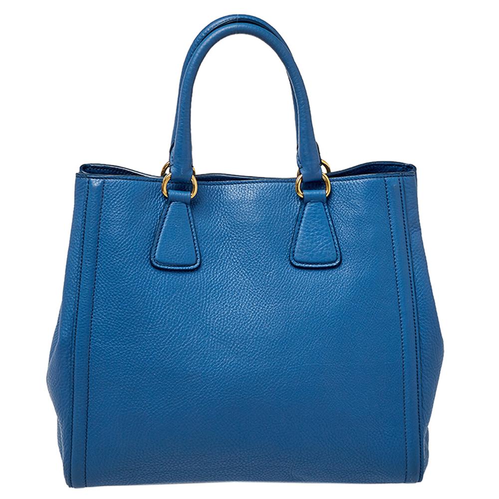 This elegant tote from Prada is crafted from Vitello Daino leather and is perfect for daily use. The bag features double handles, protective metal feet, and gold-tone hardware. The nylon-lined interior is spacious enough to hold all your