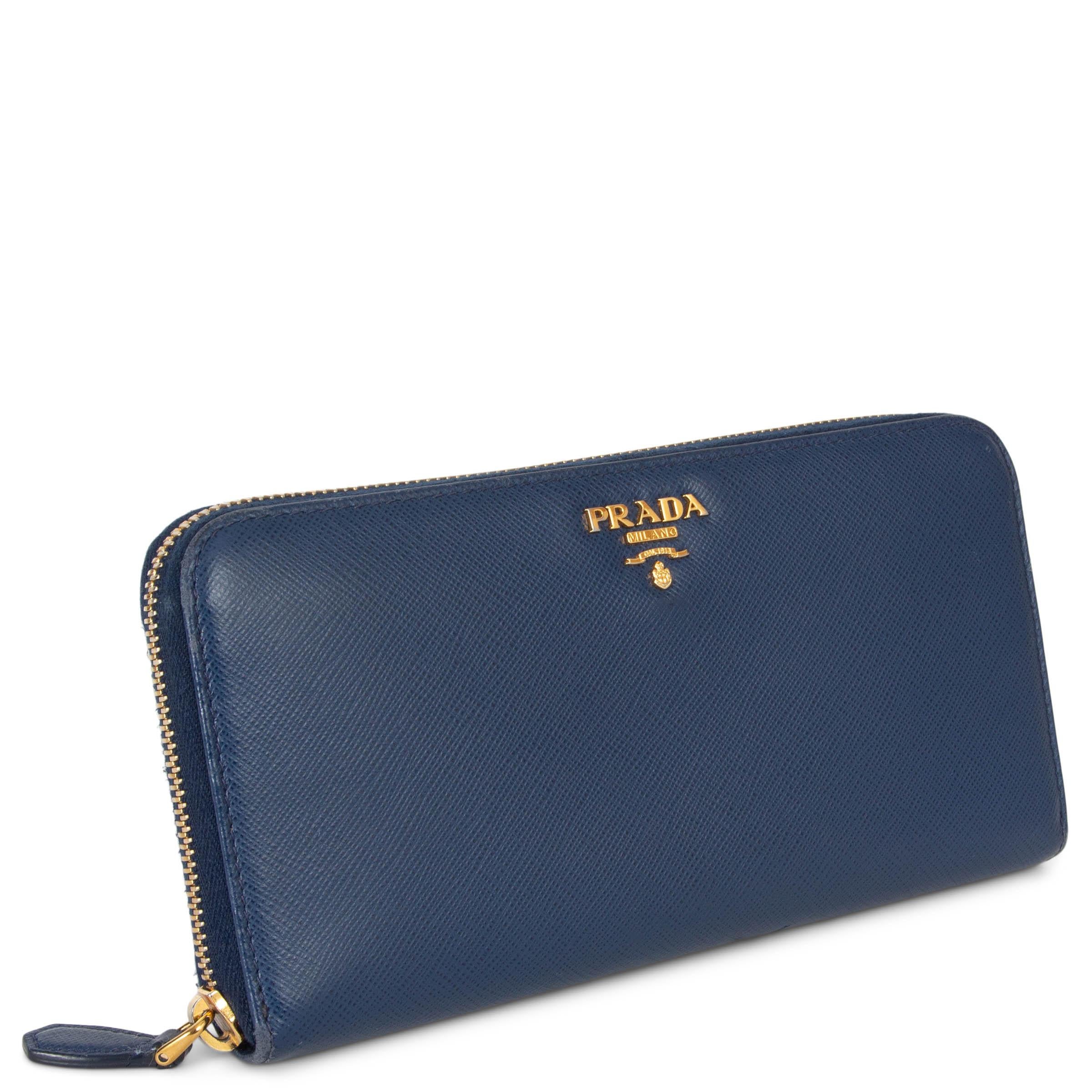 This 100% authentic Prada large wallet in Bluette (navy blue) Saffiano leather is a timeless accessory that combines elegance with functionality. Adorned with a gold-tone metal logo and hardware, it exudes classic sophistication. The wallet closes