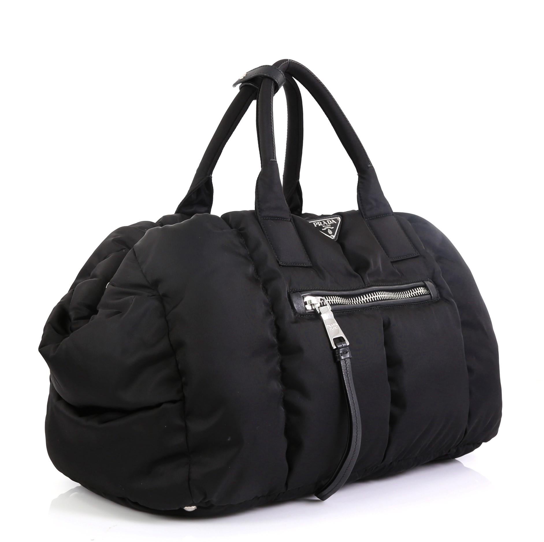 This Prada Bomber Convertible Tote Tessuto Large, crafted in black tessuto nylon, features dual-rolled handles, exterior zip pockets, and silver-tone hardware. Its top zip closure opens to a black nylon interior with zip and slip pockets.