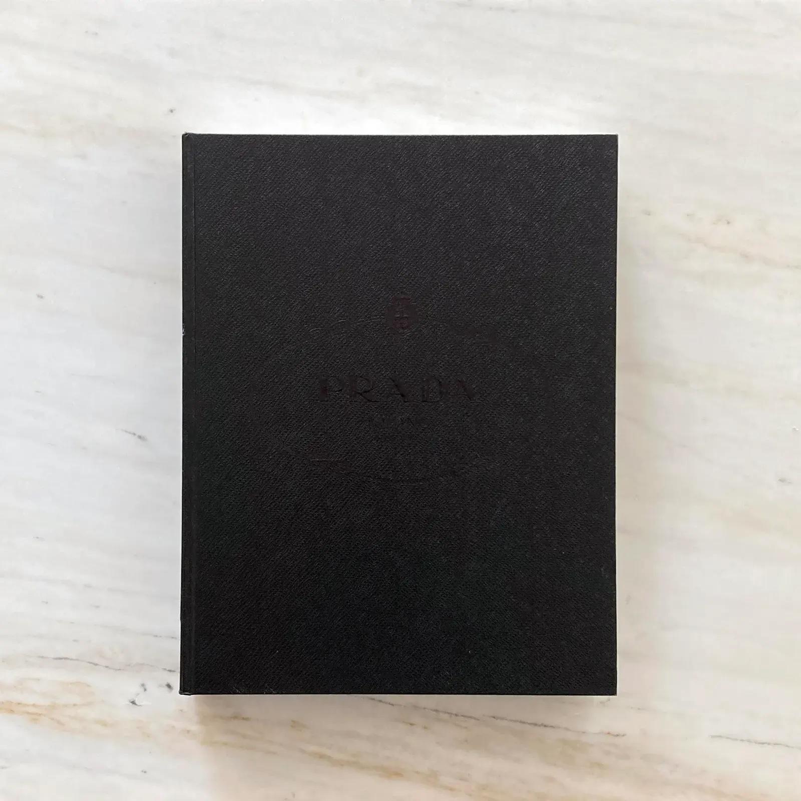 Beautiful Prada Book, étui et couverture en faux cuir texturé saffiano, ce livre est rempli de centaines de magnifiques photos retraçant l'histoire de Prada, le développement des idées, les processus de production, les campagnes publicitaires et