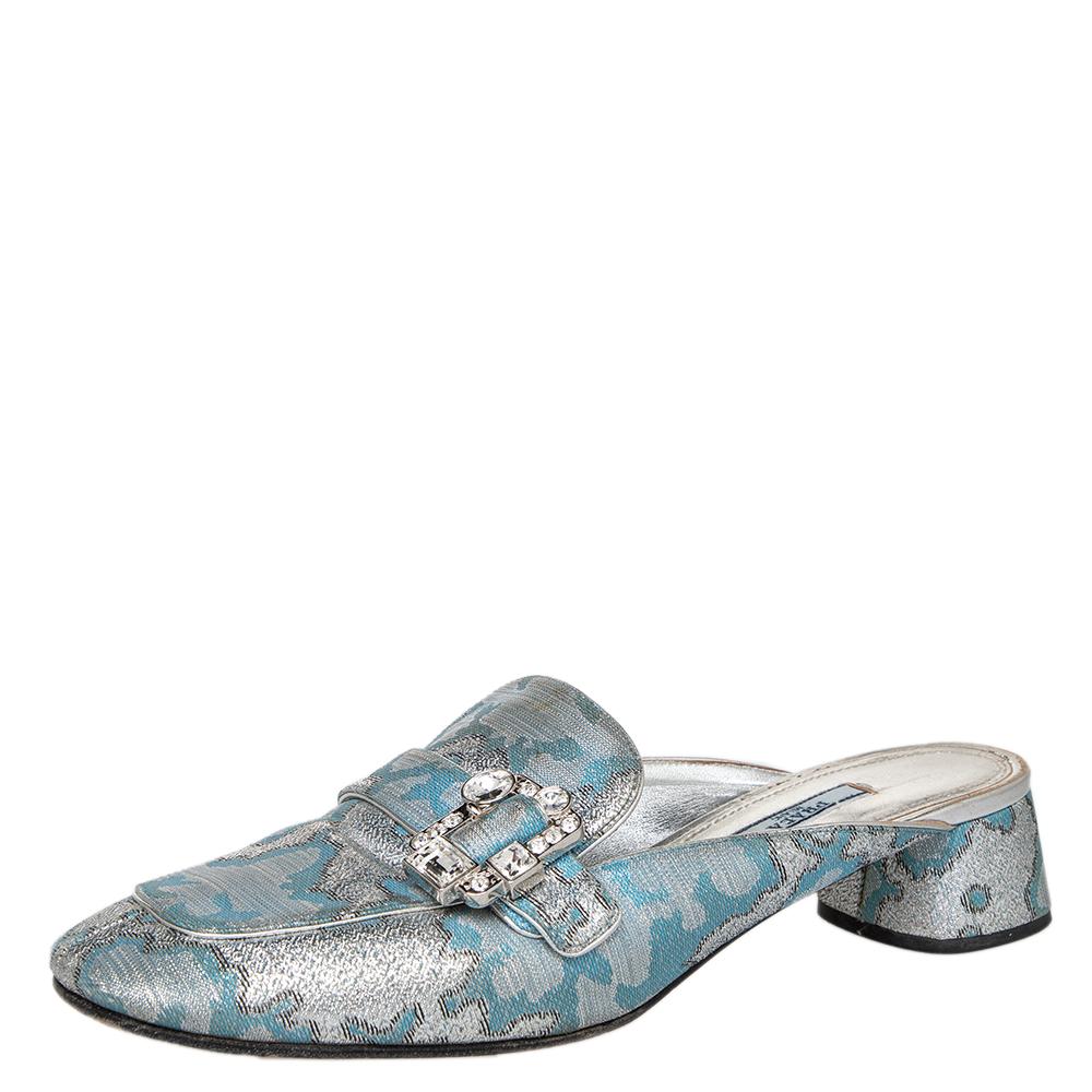 Prada's collections are a testament to the label's opulent and glamorous aesthetics. These mule sandals have been draped in brocade fabric that comes in silver and blue shades. They have been designed in a round-toe silhouette and accentuated with