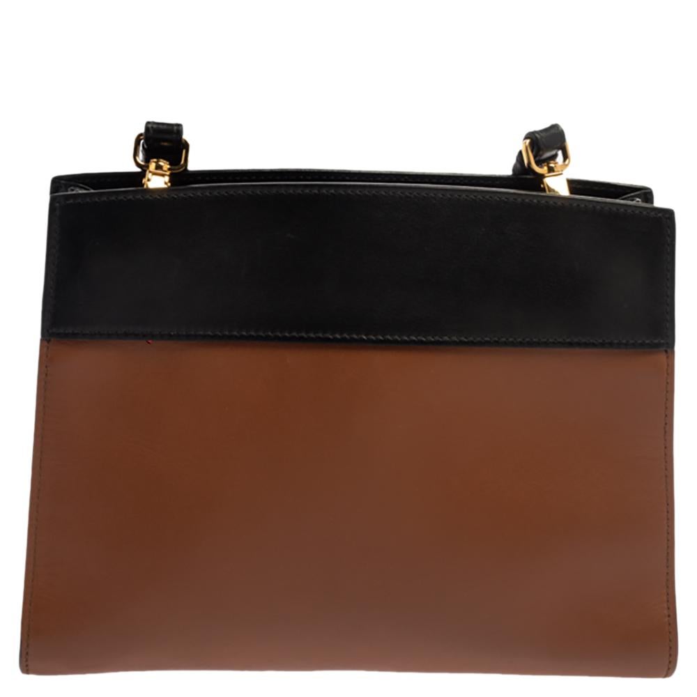 This elegant Prada bag is perfect for everyday use. Crafted from leather in black and brown hues, the bag comes with the brand label in gold-tone on the front, a single strap, and a structured silhouette. The bag is complete with a spacious