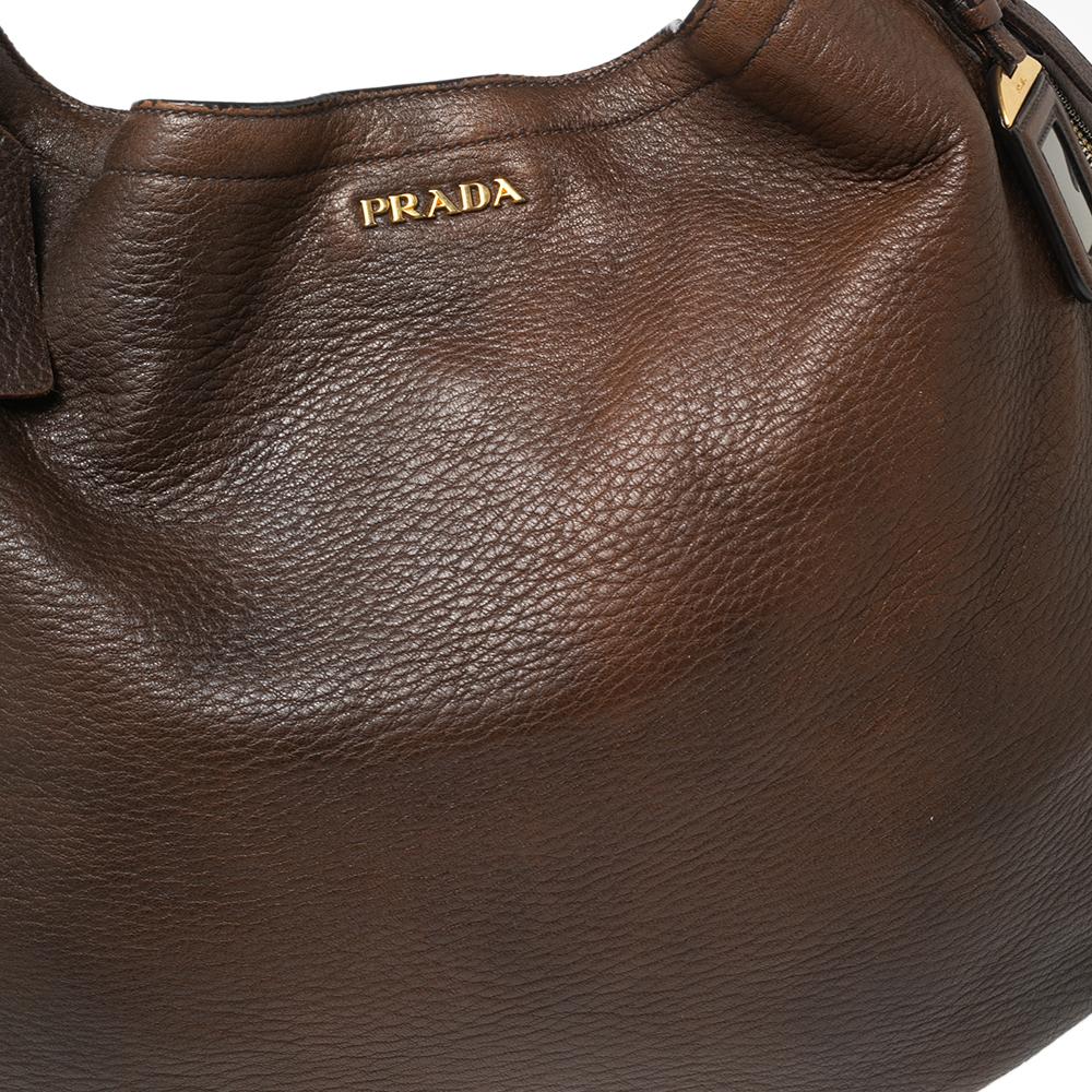This elegant hobo from Prada is crafted from brown leather and is perfect for daily use. The bag features a single handle, logo detailing the front, and gold-tone hardware. The nylon-lined interior is spacious enough to hold all your