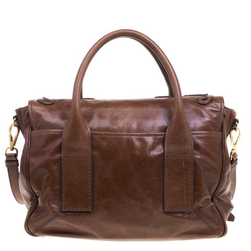 Crafted from glazed leather, this brown Prada bag has a push lock closure that opens to a suede-lined interior. The bag is equipped with dual rolled handles, a detachable shoulder strap, gold-tone hardware, and protective metal feet. Swing this