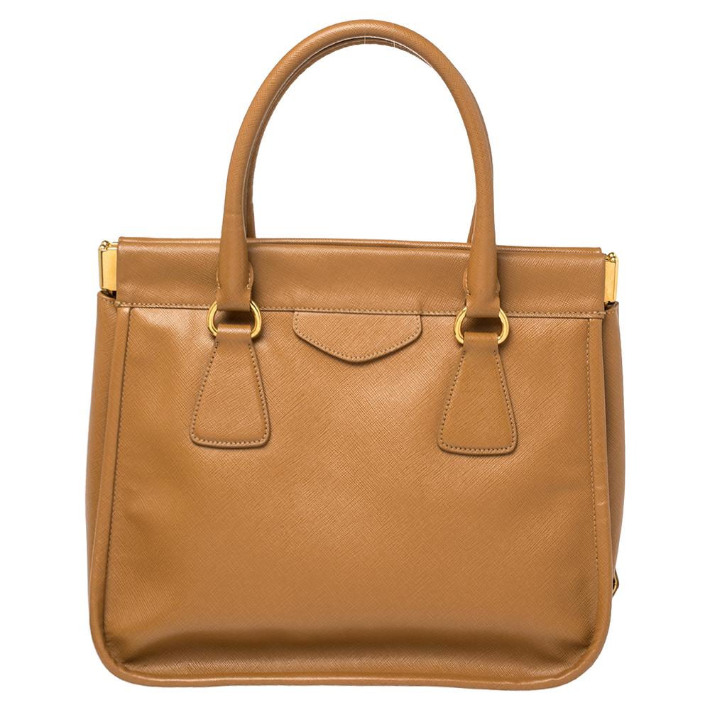 This Prada Cannella leather satchel has an alluring design. Beautifully crafted, the brown bag comes with a highly durable exterior, accompanied by gold-tone hardware, brand tag, a spacious leather interior, two handles, and protective metal feet.