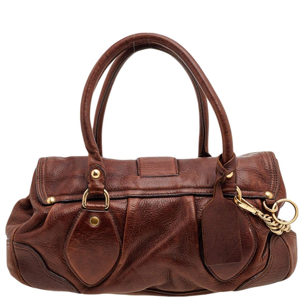 This Prada leather satchel features double top handles and a striking dragon buckle on the flap. It is equipped with a roomy fabric interior to hold your essentials and much more.

