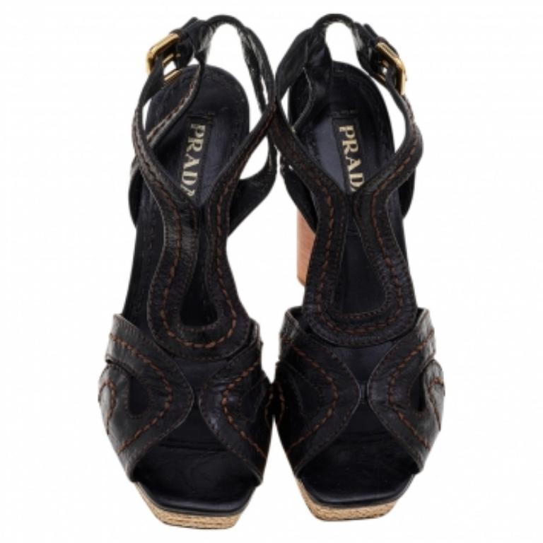 Aggiungi un elemento di glamour ed eleganza al tuo ensemble indossando questi sandali della Maison Prada. Sono realizzate in pelle marrone all'esterno e sono dotate di plateau espadrillas, tacco in legno e accessori dorati. Aumenta il tuo fattore di