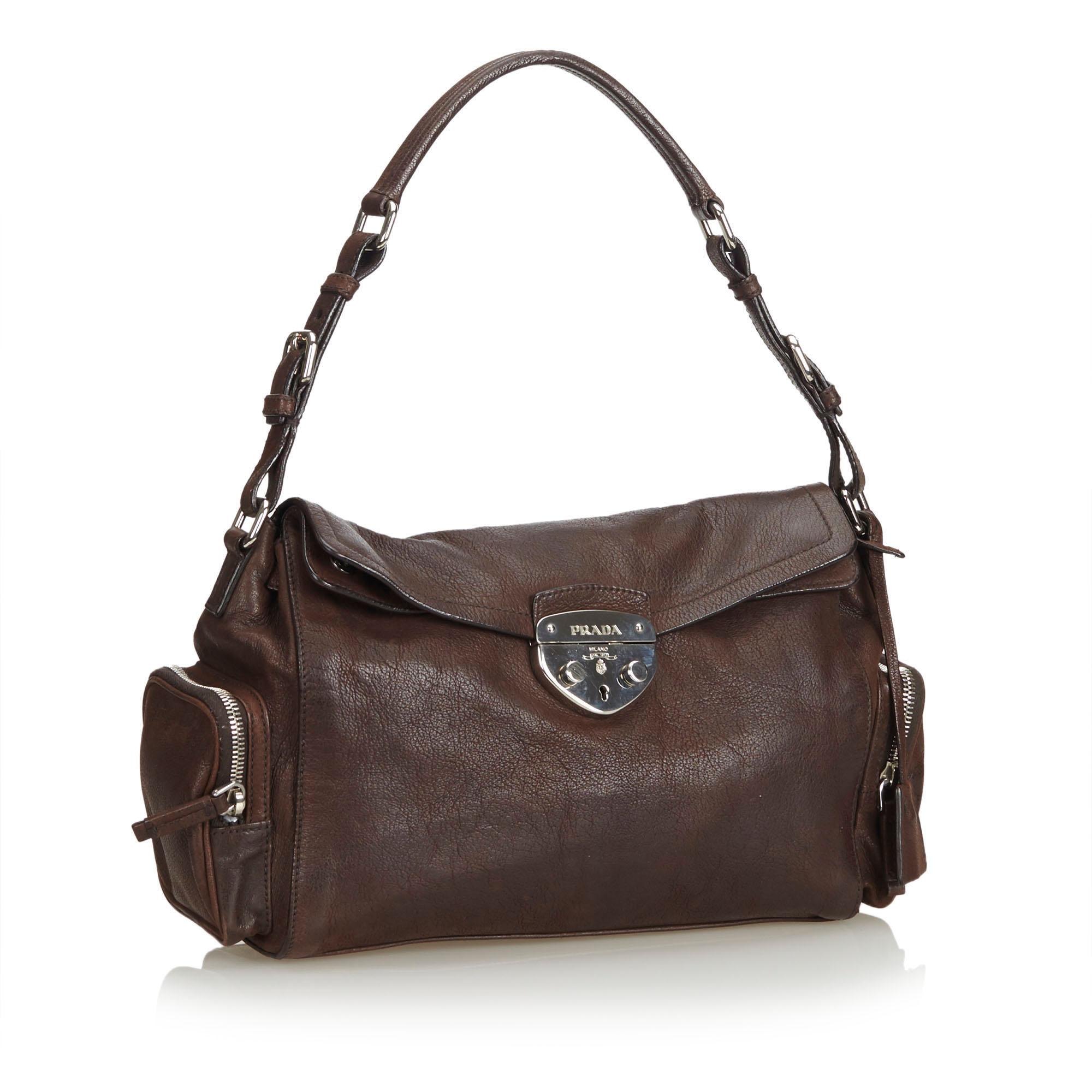 This shoulder bag features a leather body, exterior side zip pockets, exterior back zip pocket, front flap with push lock closure, flat leather strap with belt details, and an interior zip pocket. It carries as B condition rating.

Inclusions: 
Dust