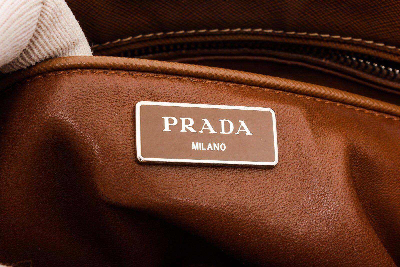 Prada Brown Saffiano Leather Double Zip Tote Bag with gold-tone hardware, three interior compartments pockets, dual top handles, leather shoulder strap, and closure.

26187MSC