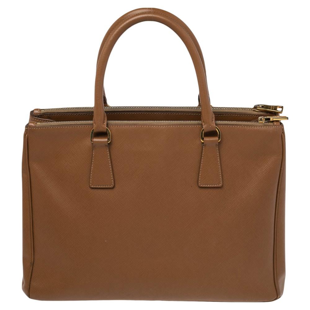 Feminine in shape and design, this Double Zip tote by Prada will be a loved addition to your closet. It has been crafted from Saffiano leather and styled minimally with gold-tone hardware. It comes with two top handles, two zip compartments, and a