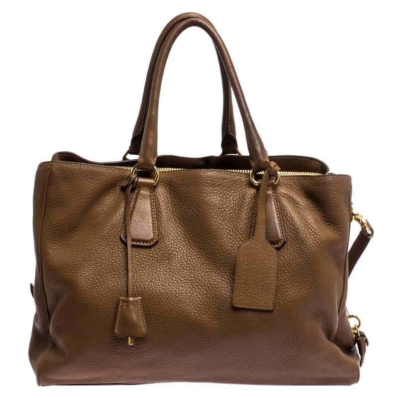 This elegant tote from Prada is crafted from soft leather and is perfect for daily use. It comes in a stunning shade of brown. The bag features double handles, protective metal feet, and a removable shoulder strap. It has a top-zip closure that