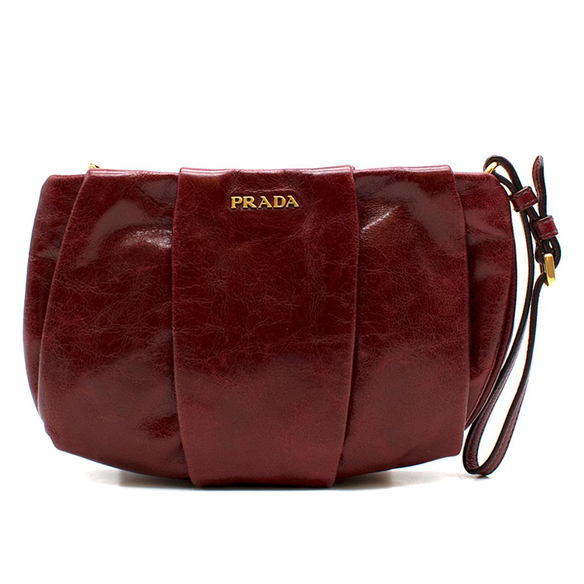 Prada burgundy leather clutch

- Burgundy, creased calf leather 
- Front and back pleated feature 
- Gold-tone metal front plaque 
- Adjustable wristlet strap
- Top zip closure, logo engraved zip tab
- Logo jacquard lining
- Comes with a box.