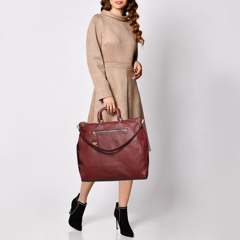 This super classy and stunning tote exudes brilliance and magnificent craftsmanship. It has a leather exterior adorned in a burgundy hue, zip pockets at the front and back, two handles, and a spacious fabric interior. This opulent bag will surely