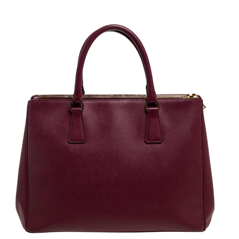 High on style and class, this Galleria Double Zip tote by Prada will be a cherished addition to your closet. It has been crafted from Saffiano Lux leather in a burgundy shade and styled minimally with gold-tone hardware. It comes with dual handles