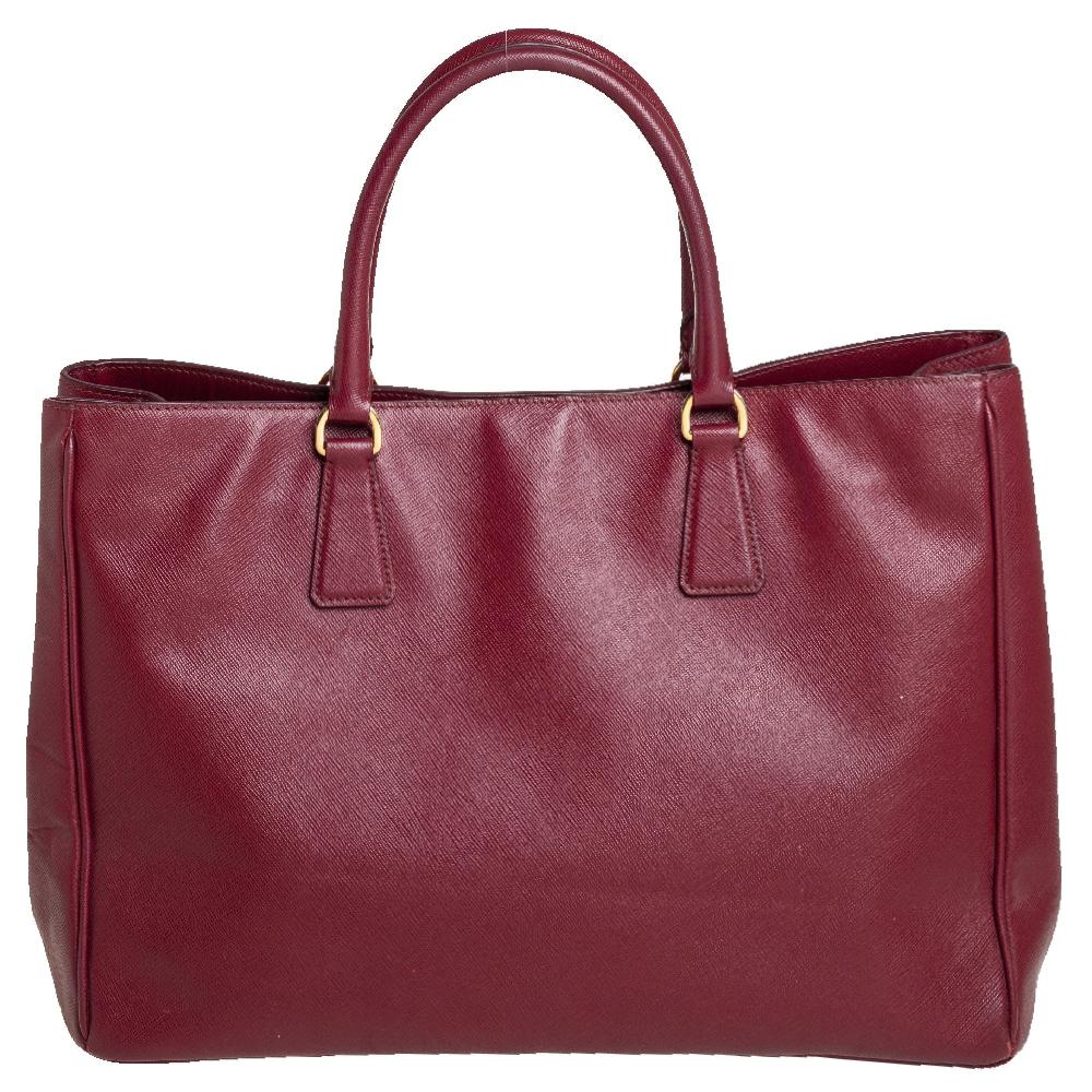 Loved for its classic appeal and functional design, Galleria is one of the most iconic and popular bags from the house of Prada. This beauty in burgundy is crafted from Saffiano leather and is equipped with two top handles, the brand logo at the