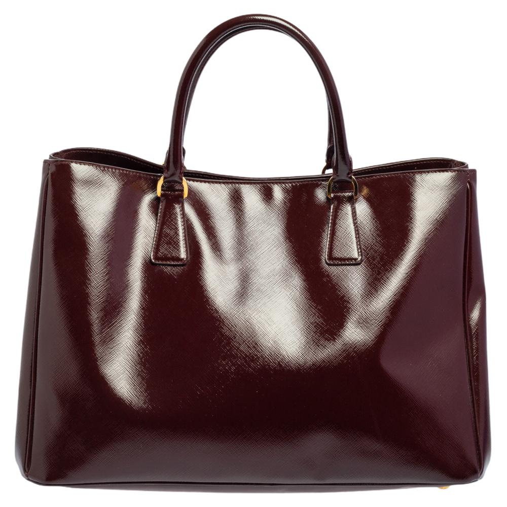 High in appeal and style, this tote is a Prada creation. It has been crafted from Saffiano Vernice leather and shaped to exude class and luxury. The bag comes with two handles and a spacious nylon interior for your ease. Protective metal feet and