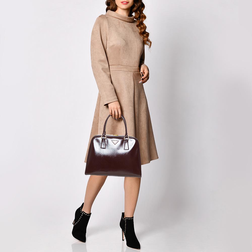 High in appeal and style, this satchel is a Prada creation. It has been crafted from Saffiano lux patent leather and shaped to exude class and luxury. The bag is designed with a gold-tone clasp on the top metal frame and comes with two handles and a