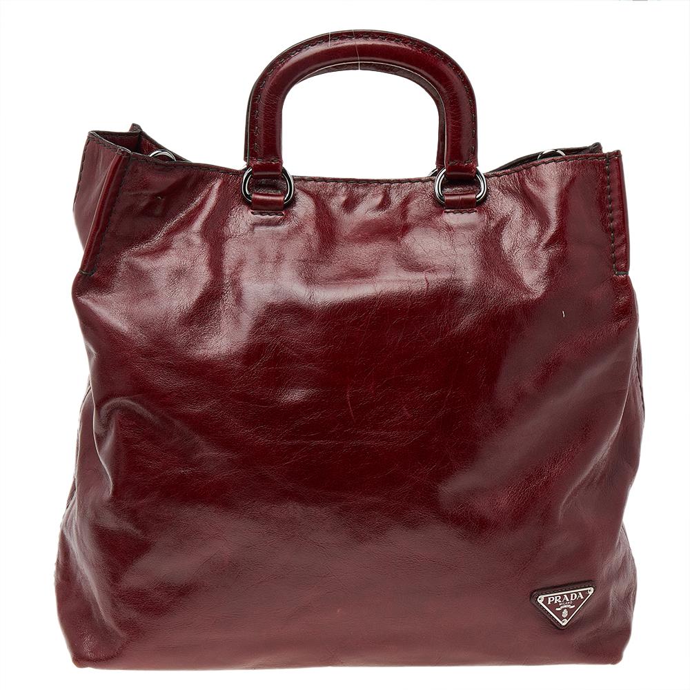 This Prada shopper tote is great for everyday use. Crafted from quality Vitello Daino leather, it comes in a shade of burgundy. It has dual handles, a shoulder strap, and silver-tone hardware. The bag opens to a nylon-lined interior that is equipped