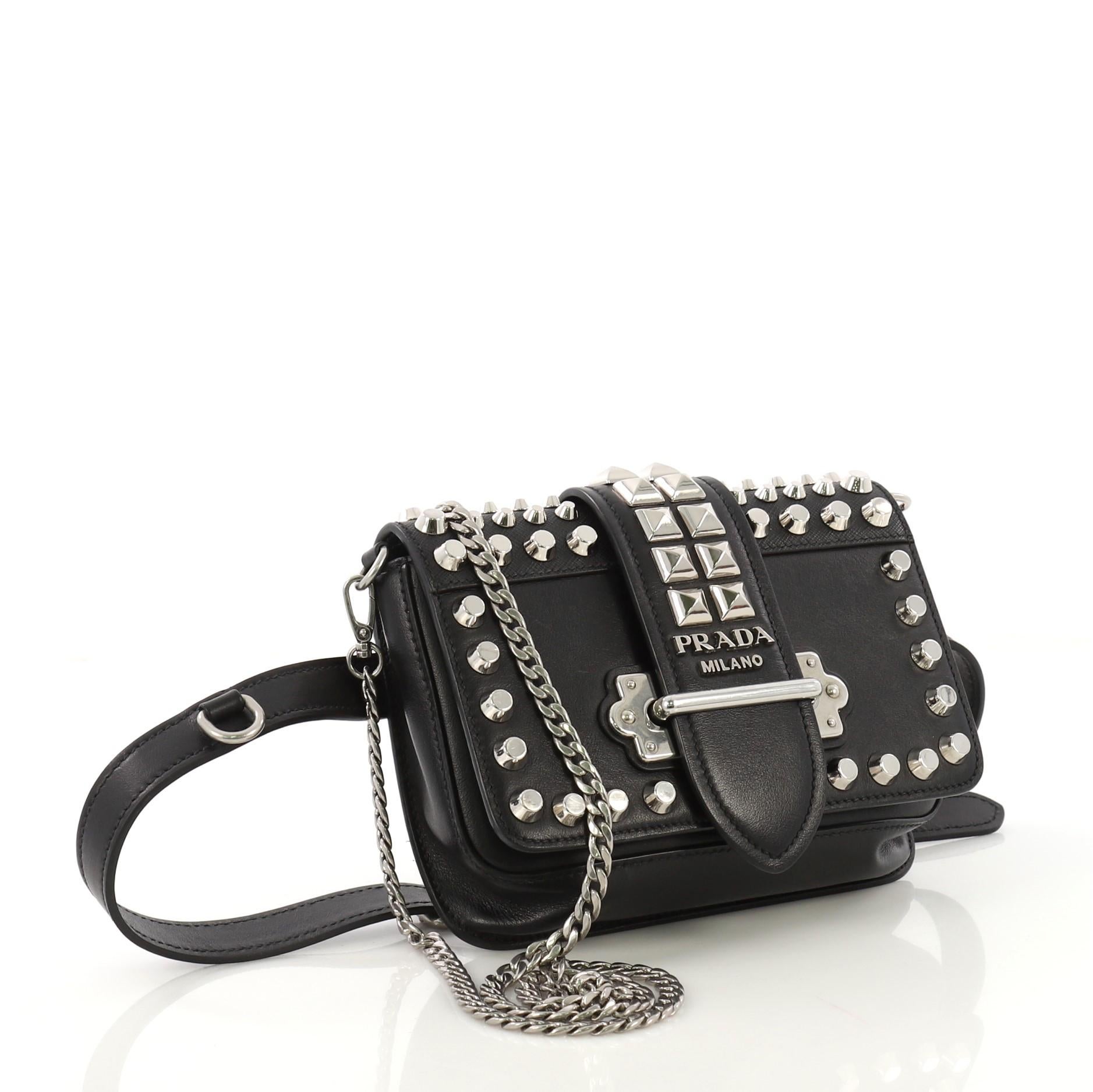 This Prada Cahier Belt Bag Studded City Calf with Saffiano Leather Small, crafted in black studded city calf with saffiano leather, features chain link strap, adjustable belt strap, stud embellishments, and silver-tone hardware. Its front flap with