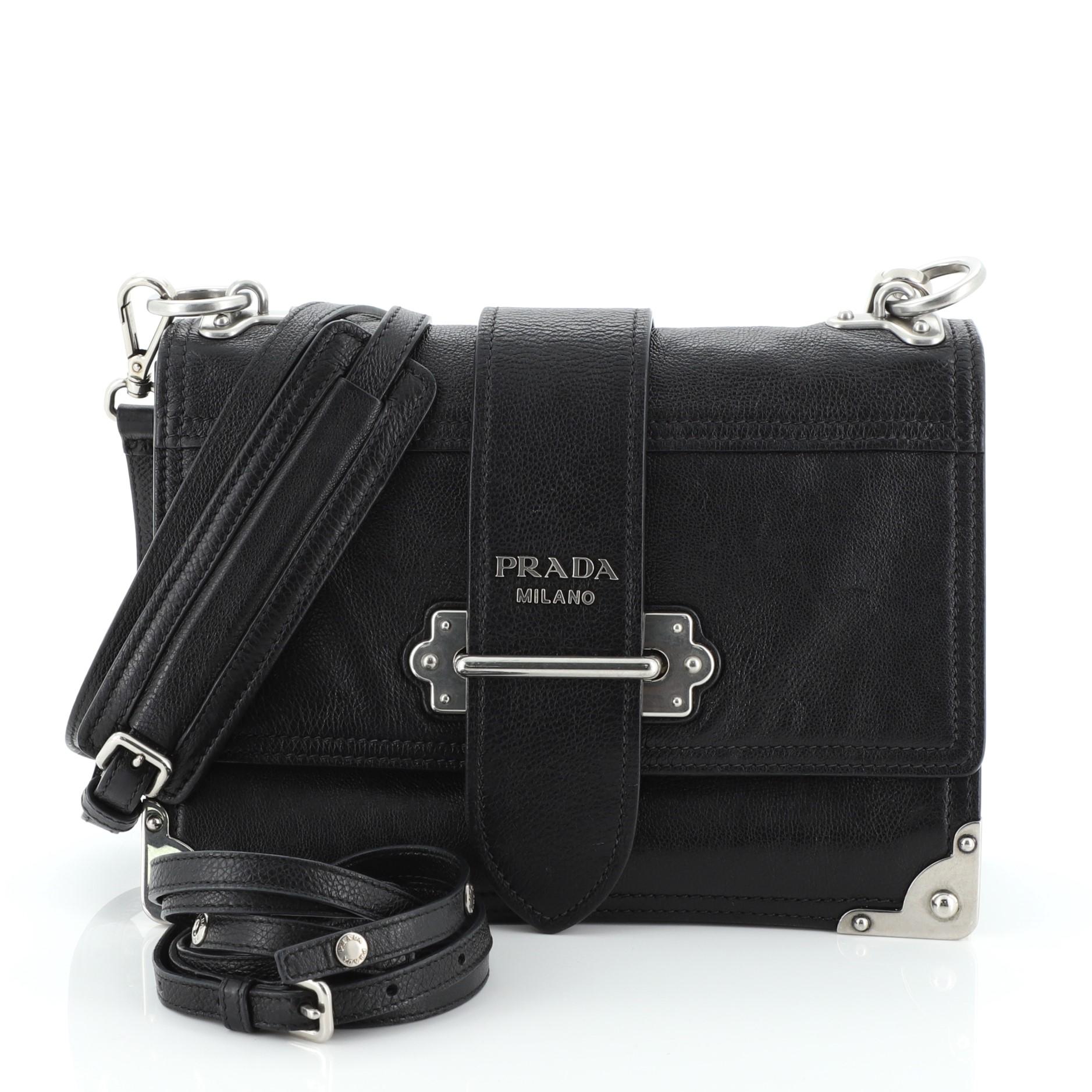 This Prada Cahier Convertible Shoulder Bag City Calf Medium, crafted from black city calf leather, features a flat leather strap, metal hardware trim, and silver-tone hardware. Its buckle closure opens to a blue suede interior with side zip and slip