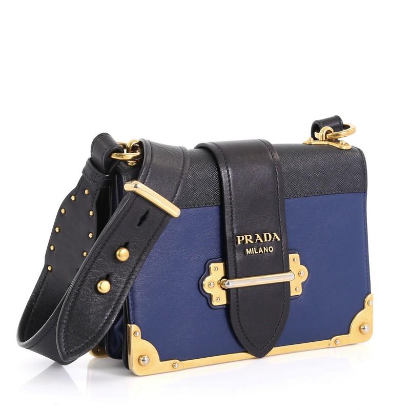 This Prada Cahier Crossbody Bag City Calf and Saffiano Leather Small, crafted from blue city calf and saffiano leather, features adjustable shoulder strap, metal hardware trim, and gold-tone hardware. Its buckle closure opens to a black leather