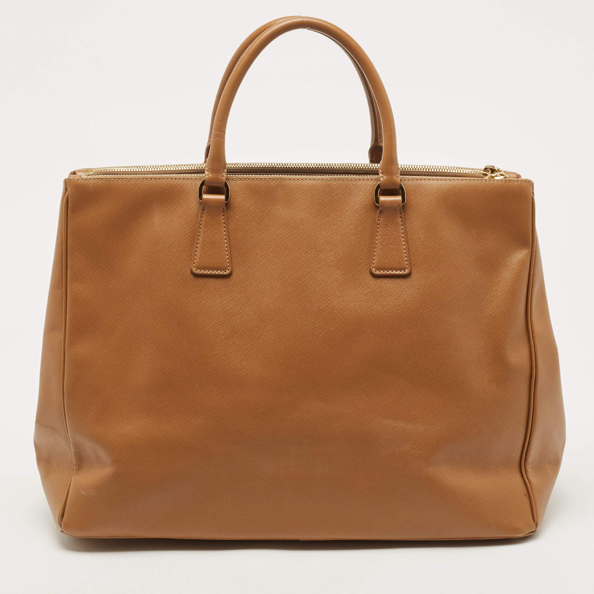 Feminine in shape and grand on design, this Double Zip tote by Prada will be a loved addition to your closet. It has been crafted from Saffiano lux leather and styled minimally with gold-tone hardware. It comes with two top handles, two zip