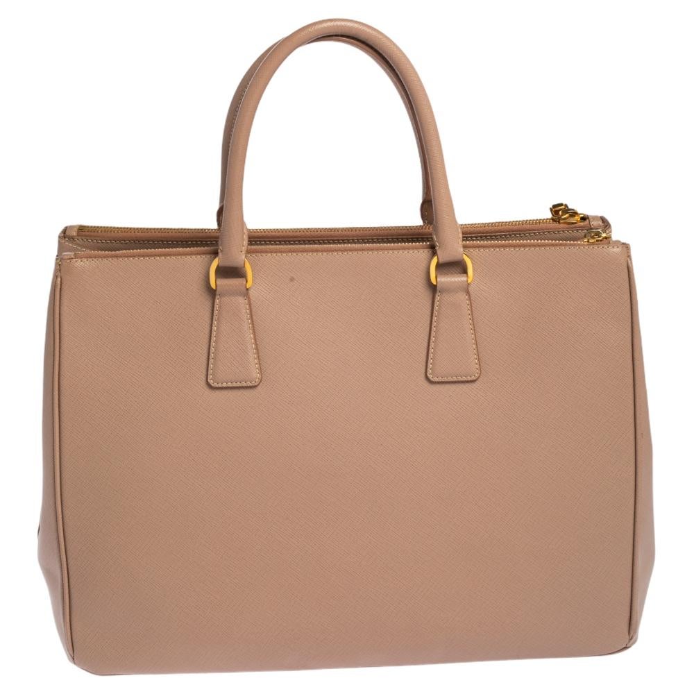 Loved for its classic appeal and functional design, Galleria is one of the most iconic and popular bags from the house of Prada. This beauty in beige is crafted from leather and is equipped with two top handles, the brand logo at the front and a