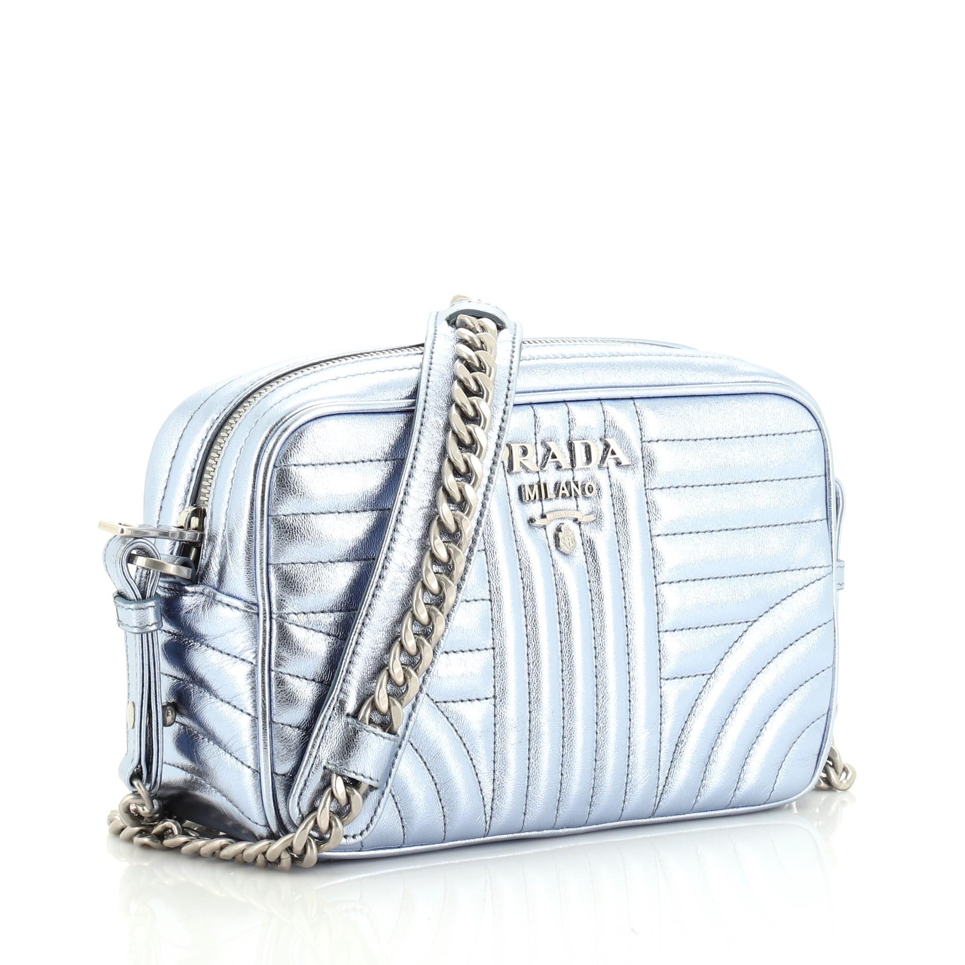This Prada Camera Bag Diagramme Quilted Leather Small, crafted from black metallic quilted leather, features a chain link strap and gold-tone hardware. Its zip closure opens to a black fabric interior with slip pocket. 

Condition: Excellent. Slight