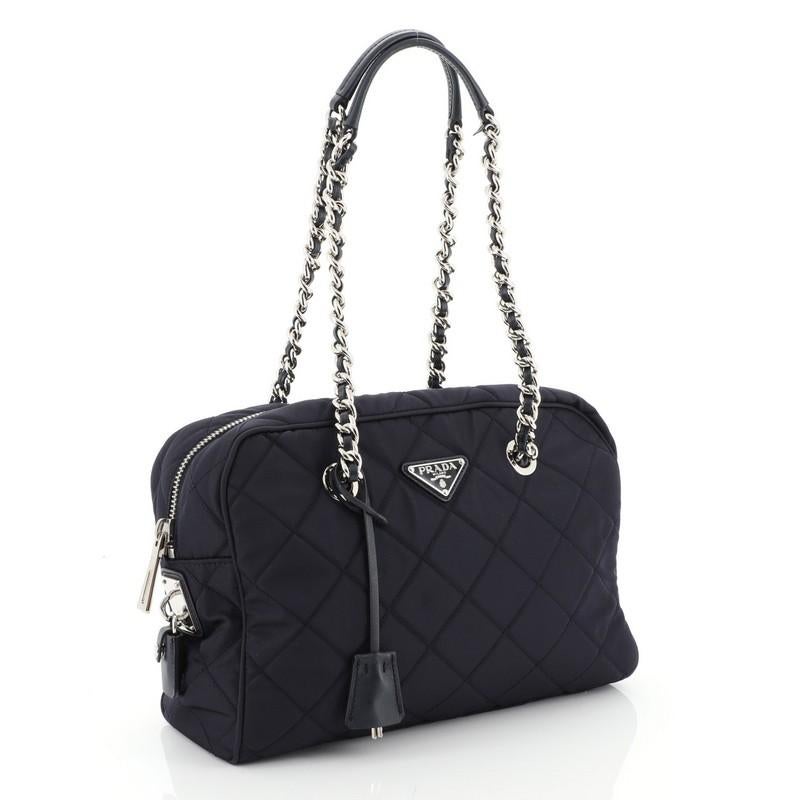 This Prada Camera Bag Quilted Tessuto Medium, crafted from blue quilted tessuto, features woven-in leather chain straps and silver-tone hardware. Its zip closure opens to a blue fabric interior with zip and slip pockets. 

Condition: Damaged. Odor