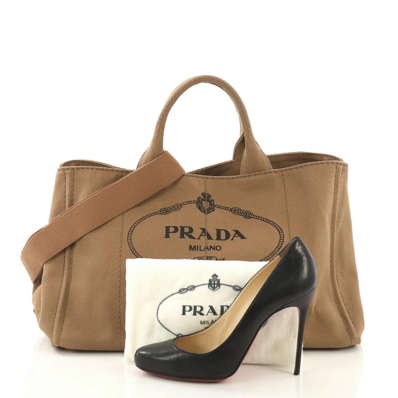 This Prada Canapa Convertible Tote Canvas Large, crafted in brown canvas, features dual top handles, side snap buttons, protective base studs, and gold-tone hardware. It opens to a brown canvas interior with side zip and slip pockets. **Note: Shoe