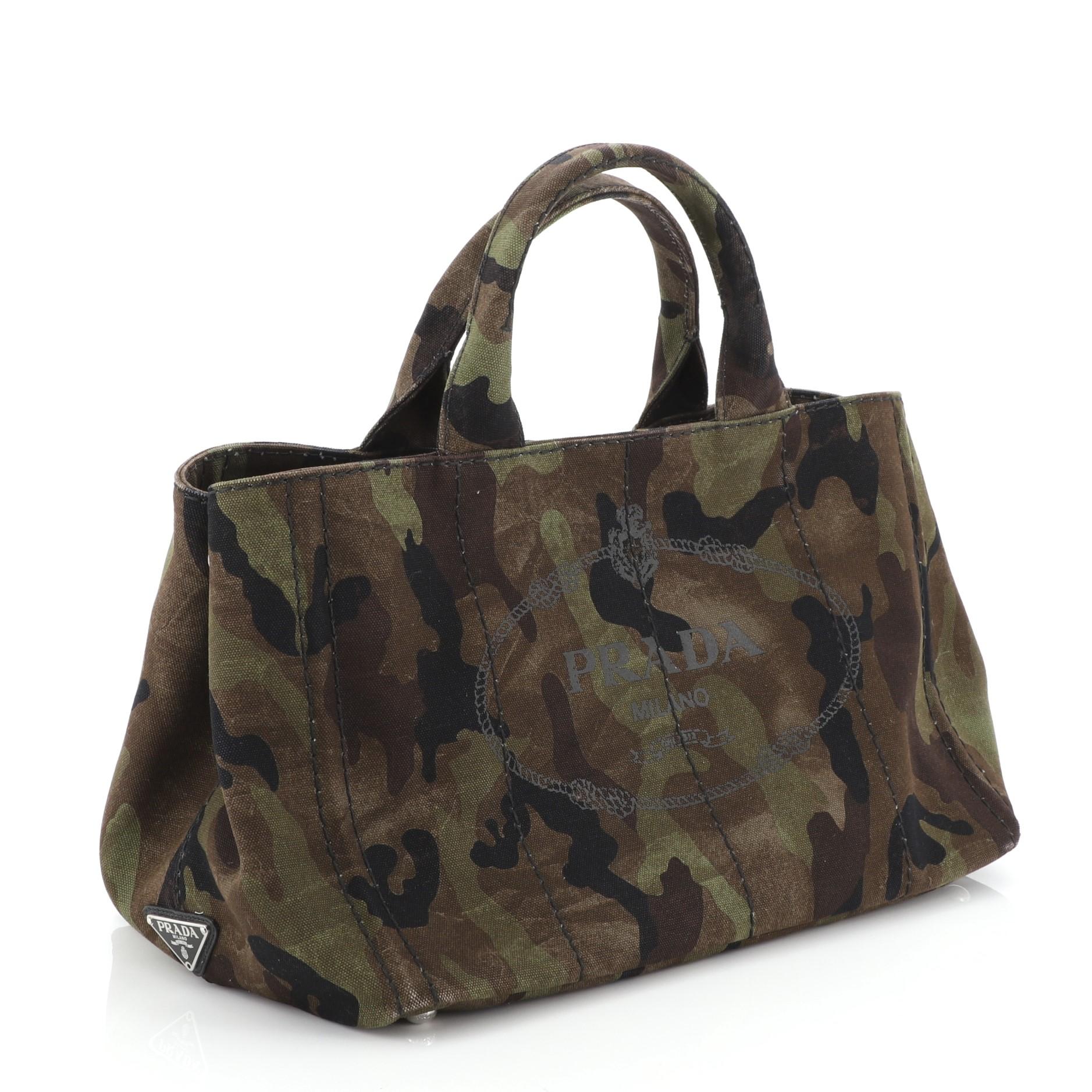 This Prada Canapa Convertible Tote Canvas Large, crafted in green printed canvas, features dual top handles, side snap buttons, and silver-tone hardware. It opens to a black fabric and canvas interior with side zip and slip pockets. 

Estimated