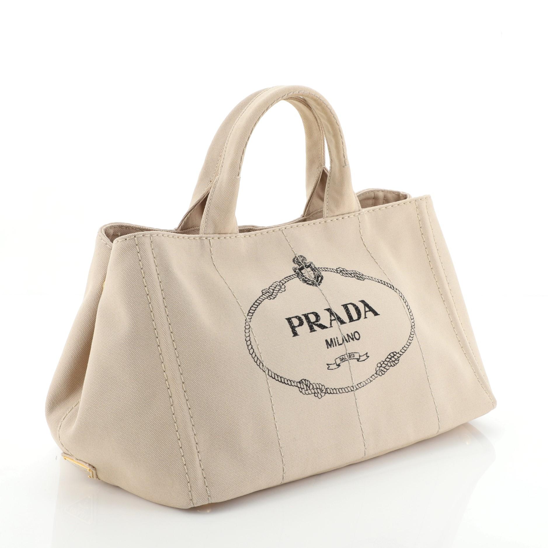 This Prada Canapa Convertible Tote Canvas Large, crafted in neutral printed canvas, features dual top handles, side snap buttons, and gold-tone hardware. It opens to a neutral fabric and canvas interior with side zip and slip pockets. 

Estimated