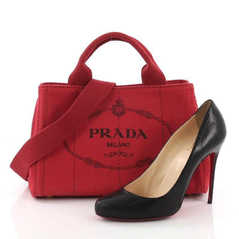 This Prada Canapa Convertible Tote Canvas Mini, crafted in red canvas, features dual top handles, side snap buttons, protective base studs, and gold-tone hardware. Its wide top opening showcases a red canvas interior with side zip and slip pockets.