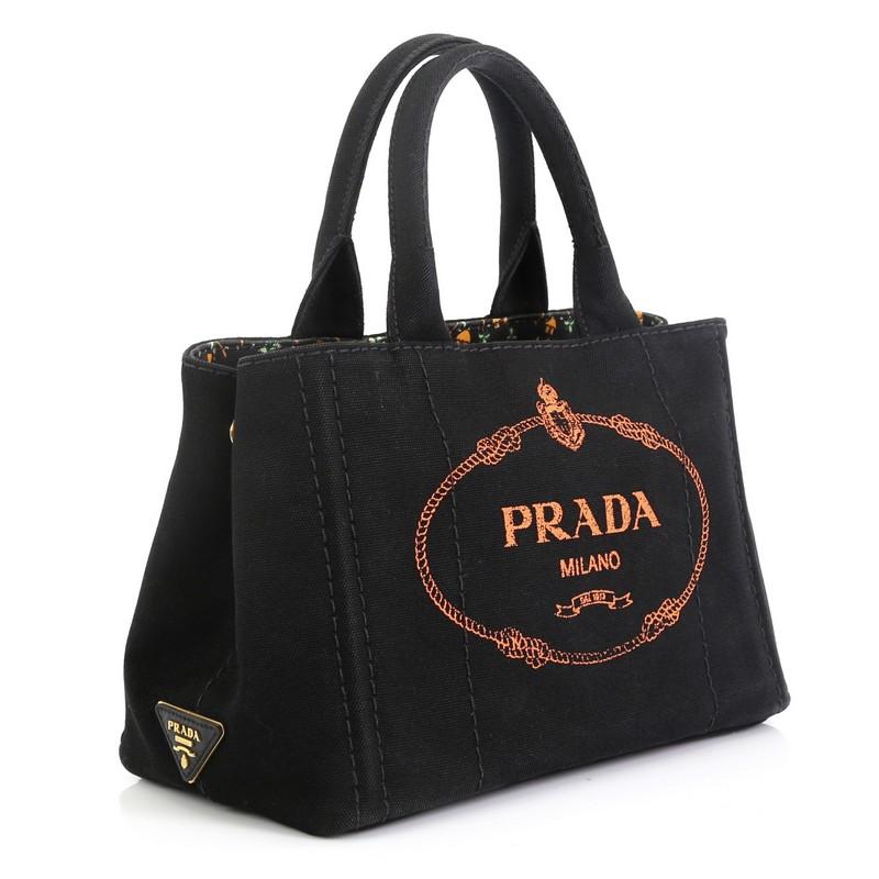 This Prada Canapa Convertible Tote Canvas Mini, crafted from black canvas, features dual rolled handles, side snap buttons, and gold-tone hardware. It opens to a black multicolor printed canvas interior with zip and slip pockets. 

Estimated Retail