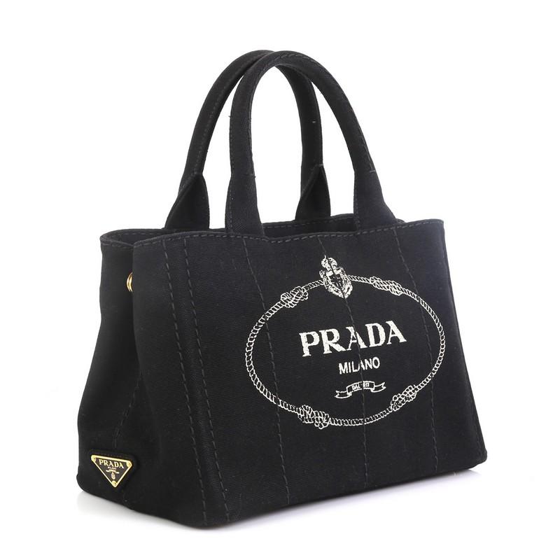 This Prada Canapa Convertible Tote Canvas Mini, crafted from black canvas, features dual rolled handles, side snap buttons, and gold-tone hardware. It opens to a black canvas interior with zip and slip pockets.

Estimated Retail Price: