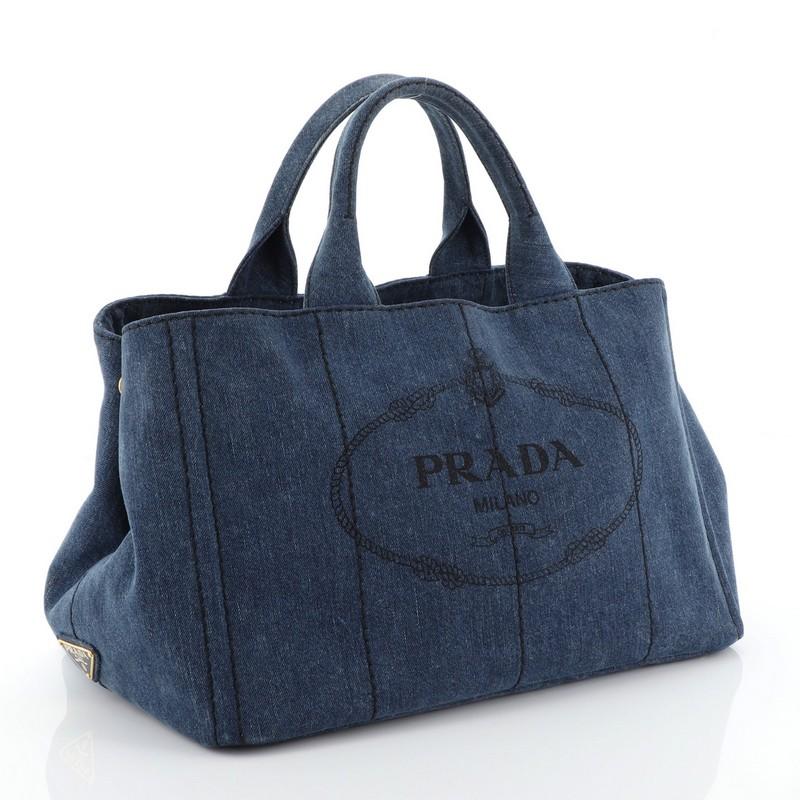 This Prada Canapa Convertible Tote Denim Medium, crafted in blue denim and canvas, features dual top handles, side snap buttons, protective base studs, and gold-tone hardware. It opens to a blue denim and canvas interior with side zip and slip