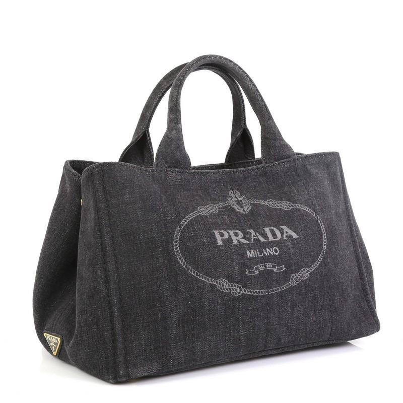 This Prada Canapa Convertible Tote Denim Medium, crafted in black denim, features dual rolled handles, side snap buttons and gold-tone hardware. Its wide top opening showcases a black denim interior with side zip and slip pockets. 

Estimated Retail