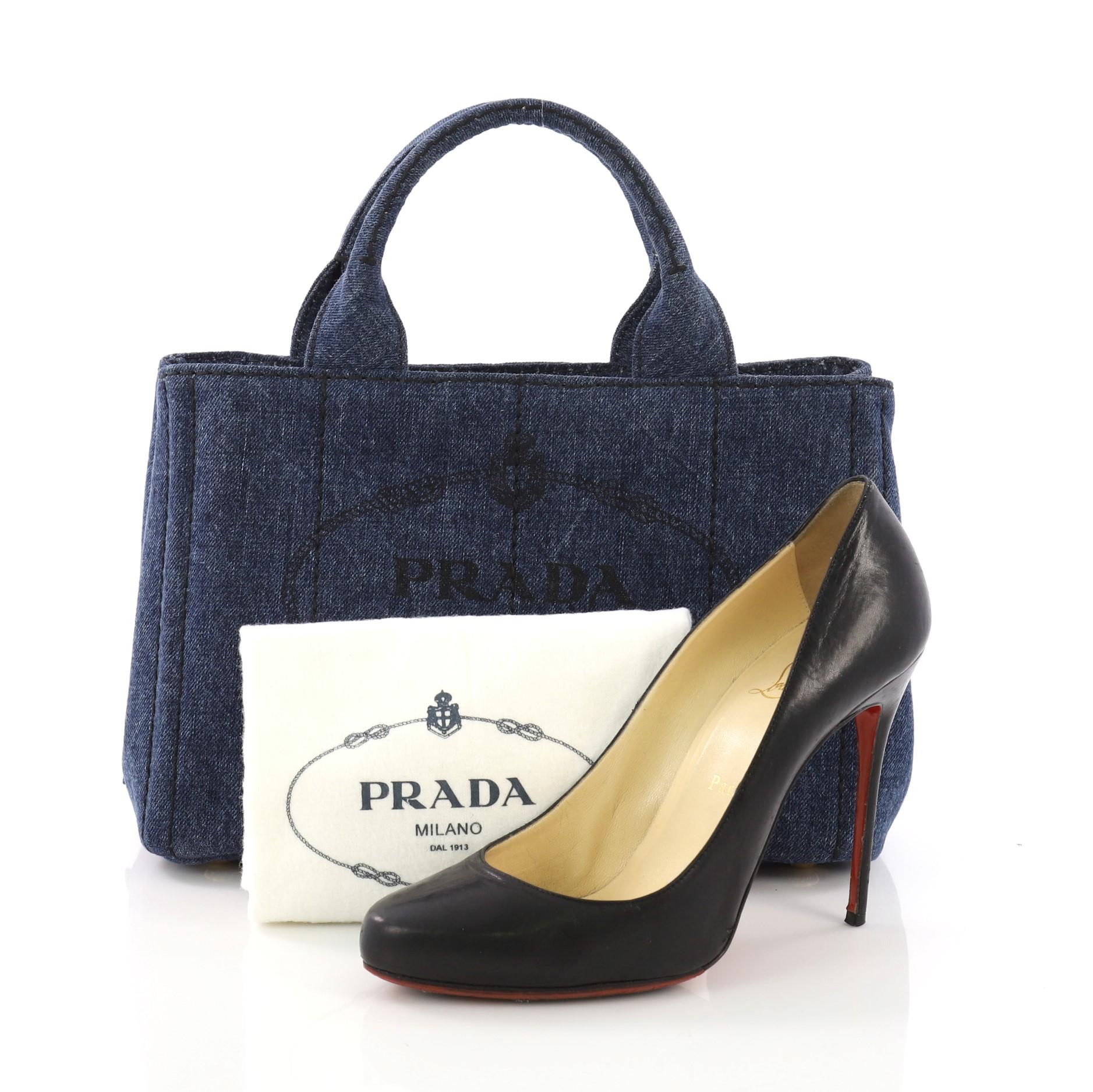 This Prada Canapa Convertible Tote Denim Mini, crafted from blue denim, features dual handles, side snap buttons, protective base studs, and gold-tone hardware. Its wide top opening showcases a blue denim interior with zip and slip pockets. **Note: