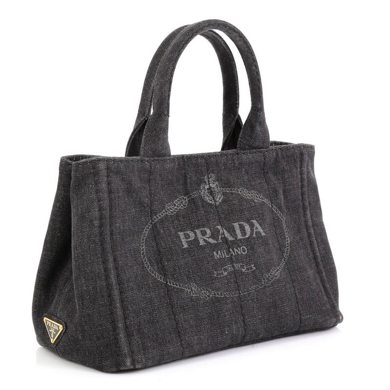 This Prada Canapa Convertible Tote Denim Mini, crafted from black denim, features dual rolled handles, side snap buttons, and gold-tone hardware. It opens to a black denim interior with zip and slip pockets. 

Estimated Retail Price: $695
Condition: