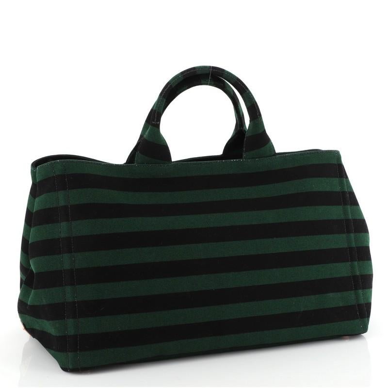 This Prada Canapa Convertible Tote Printed Canvas Large, crafted from black and green printed canvas, features dual rolled handles, side snap buttons, and gold-tone hardware. It opens to a black fabric interior with zip and slip pockets. 

Estimated