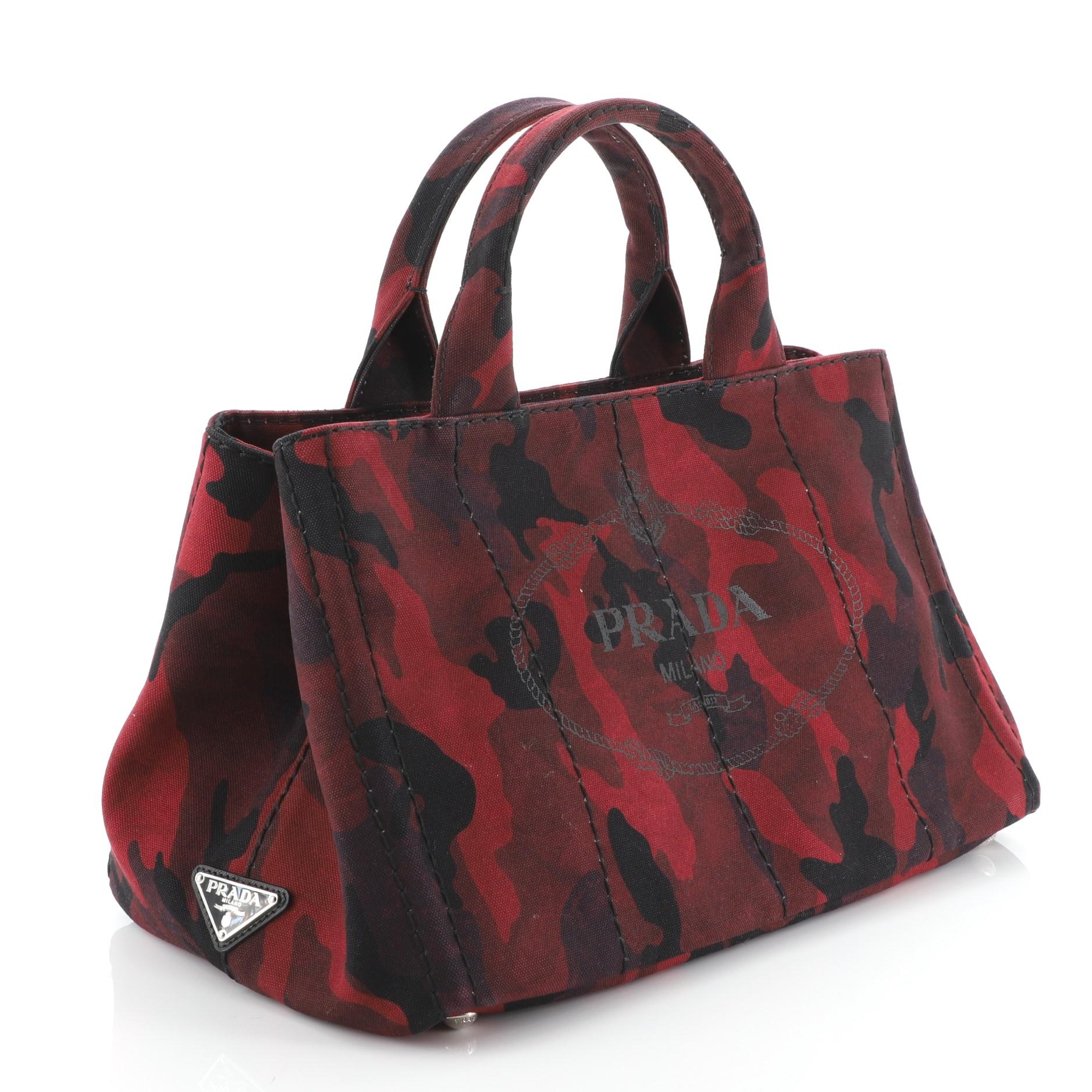 This Prada Canapa Convertible Tote Printed Canvas Medium, crafted from red printed canvas, features dual rolled handles, side snap buttons, and silver-tone hardware. It opens to a red fabric interior with zip and slip pockets. 

Estimated Retail