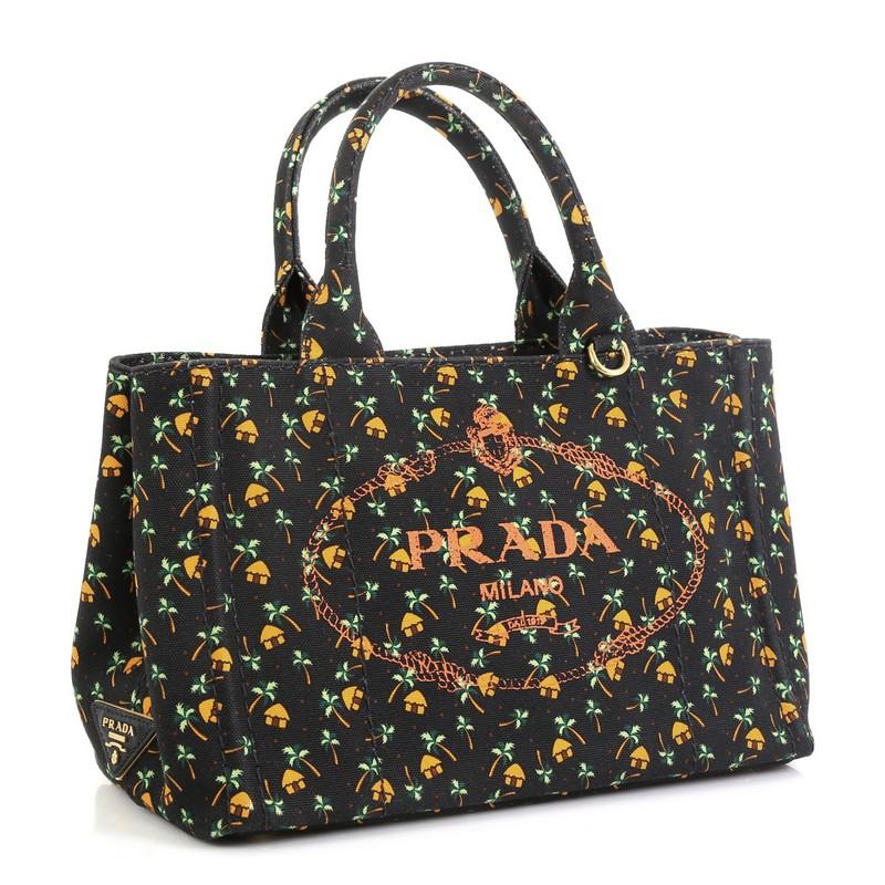 This Prada Canapa Convertible Tote Printed Canvas Mini, crafted from black and orange printed canvas, features dual rolled handles, side snap buttons, and gold-tone hardware. Its wide top opening showcases a black and orange printed fabric interior