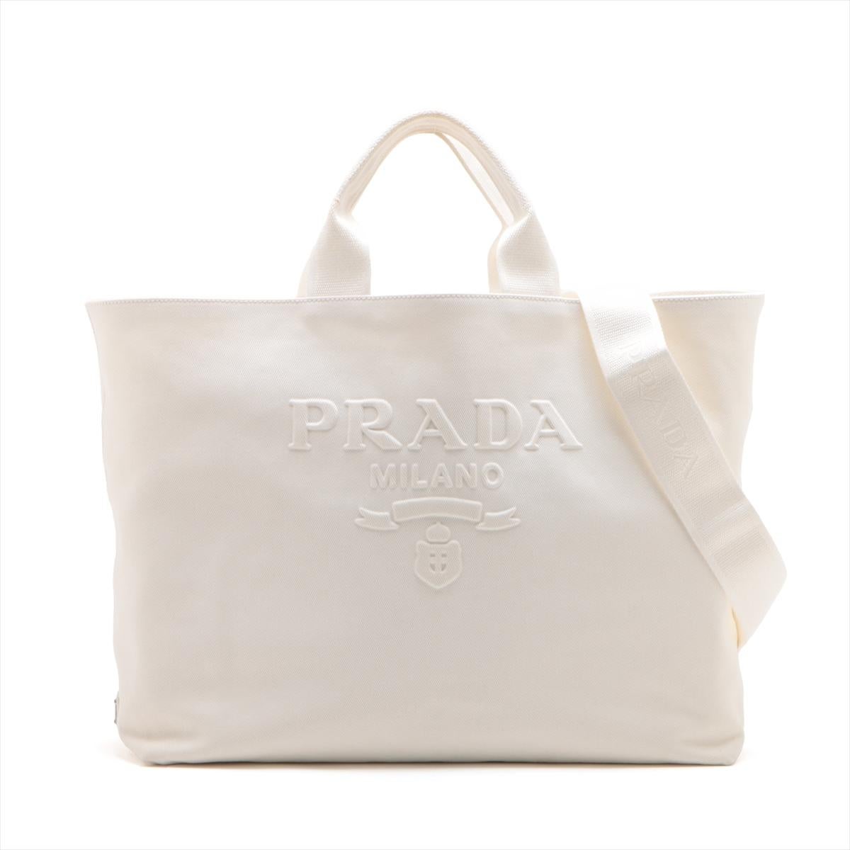 The Prada Canvas Two-Way Tote Bag in White is a stylish and versatile piece that perfectly blends casual elegance with practicality. Crafted from durable canvas, the tote features the iconic Prada logo embossed on the front, adding a touch of